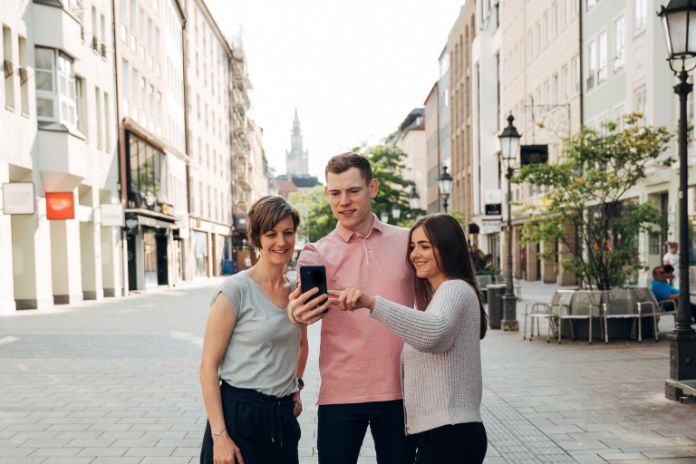 Drei Personen in der Münchner Innenstadt blicken auf ein Handydisplay