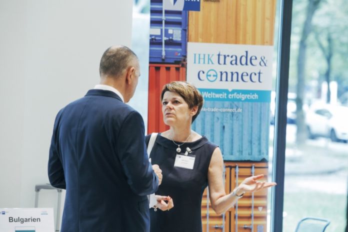 zwei Businessleute im Gespräch vor einer Stellwand mit dem Logo IHK Trade & Connect