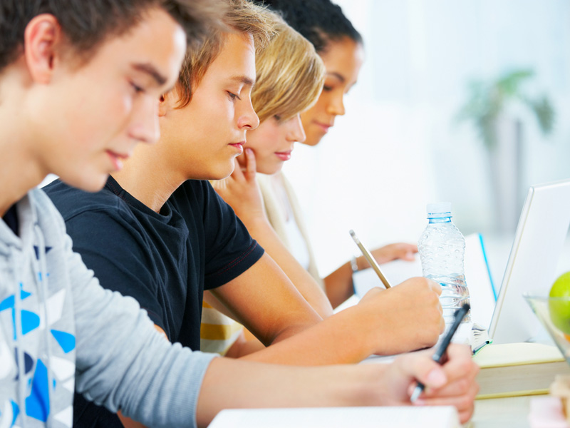 Mehrere Schüler in einer Reihe, die aufmerksam zuhören oder mitschreiben