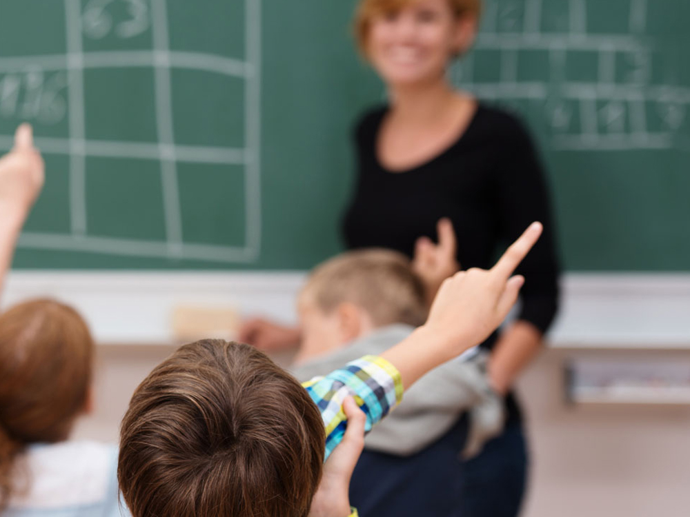 Lehrerin steht an der Tafel und Kinder melden sich.