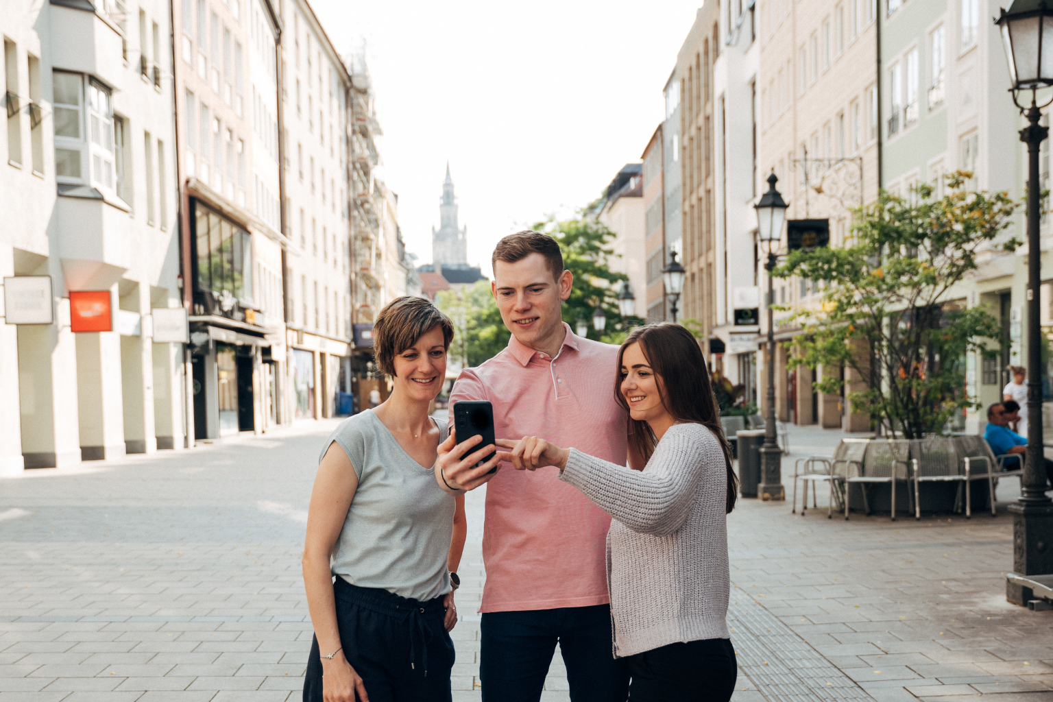 Drei Personen in der Münchner Innenstadt blicken auf ein Handydisplay