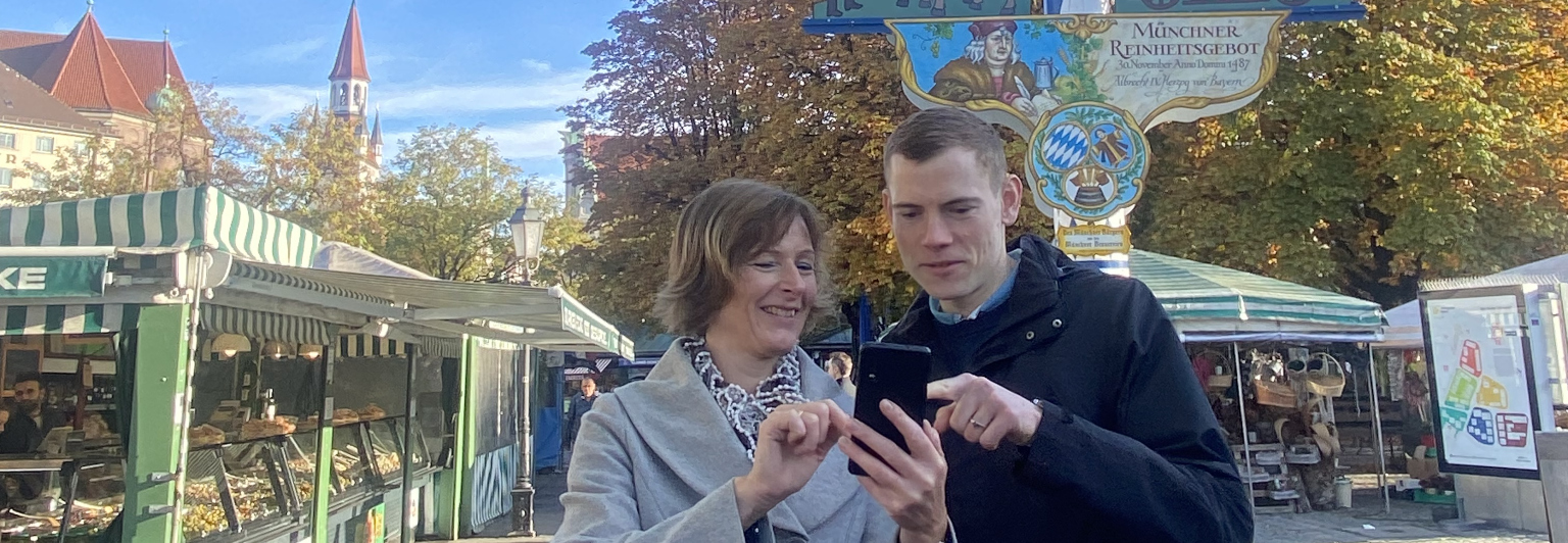 Frau und Mann mit Handy am Viktualienmarkt vor Maibaum